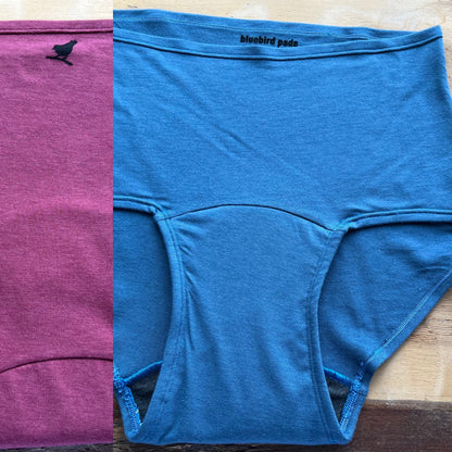 Blue underwear with 'bluebird pads' branding on a wooden surface