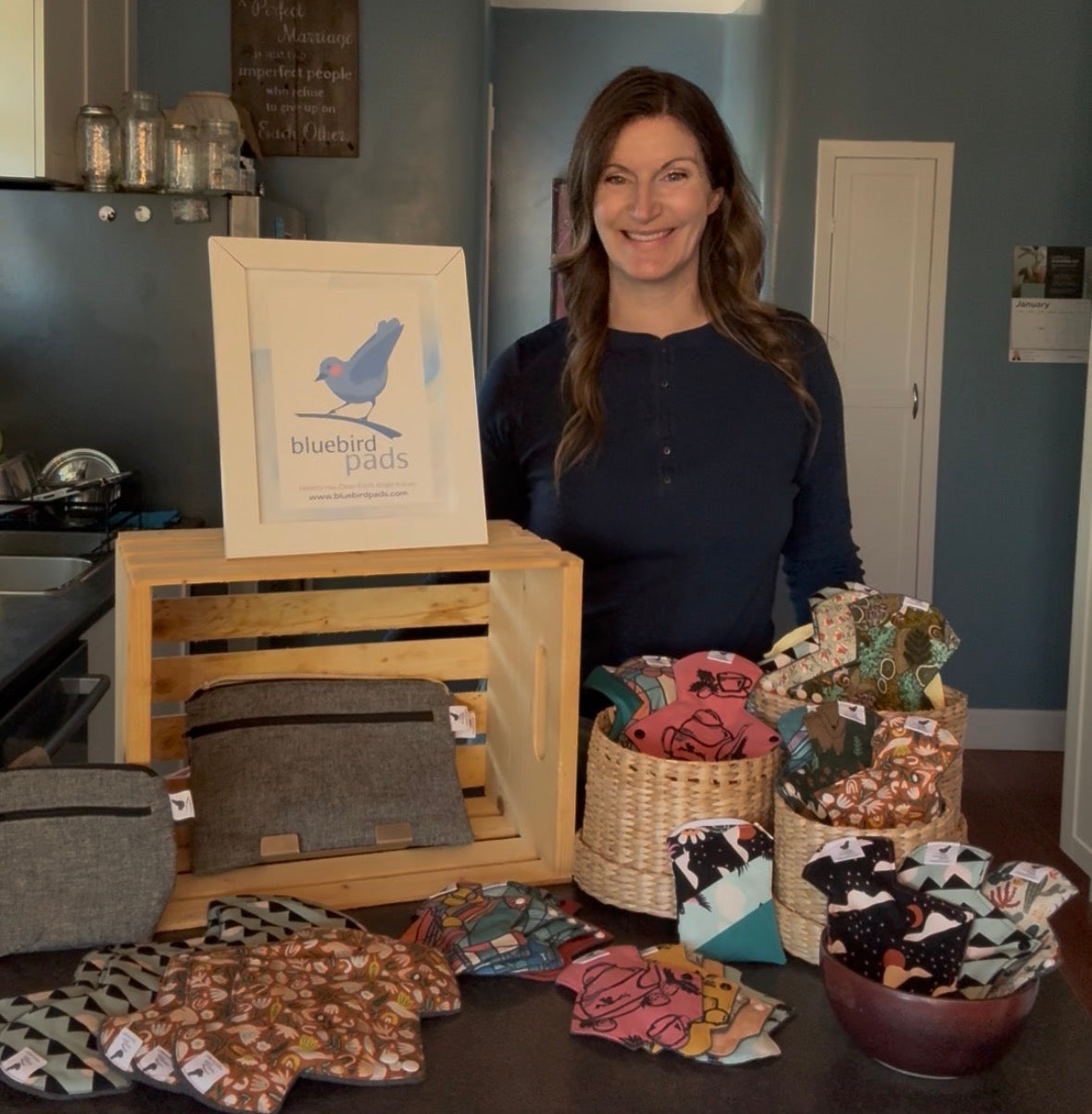 Woman standing behind a display of fabric products with 'bluebird pads' branding.